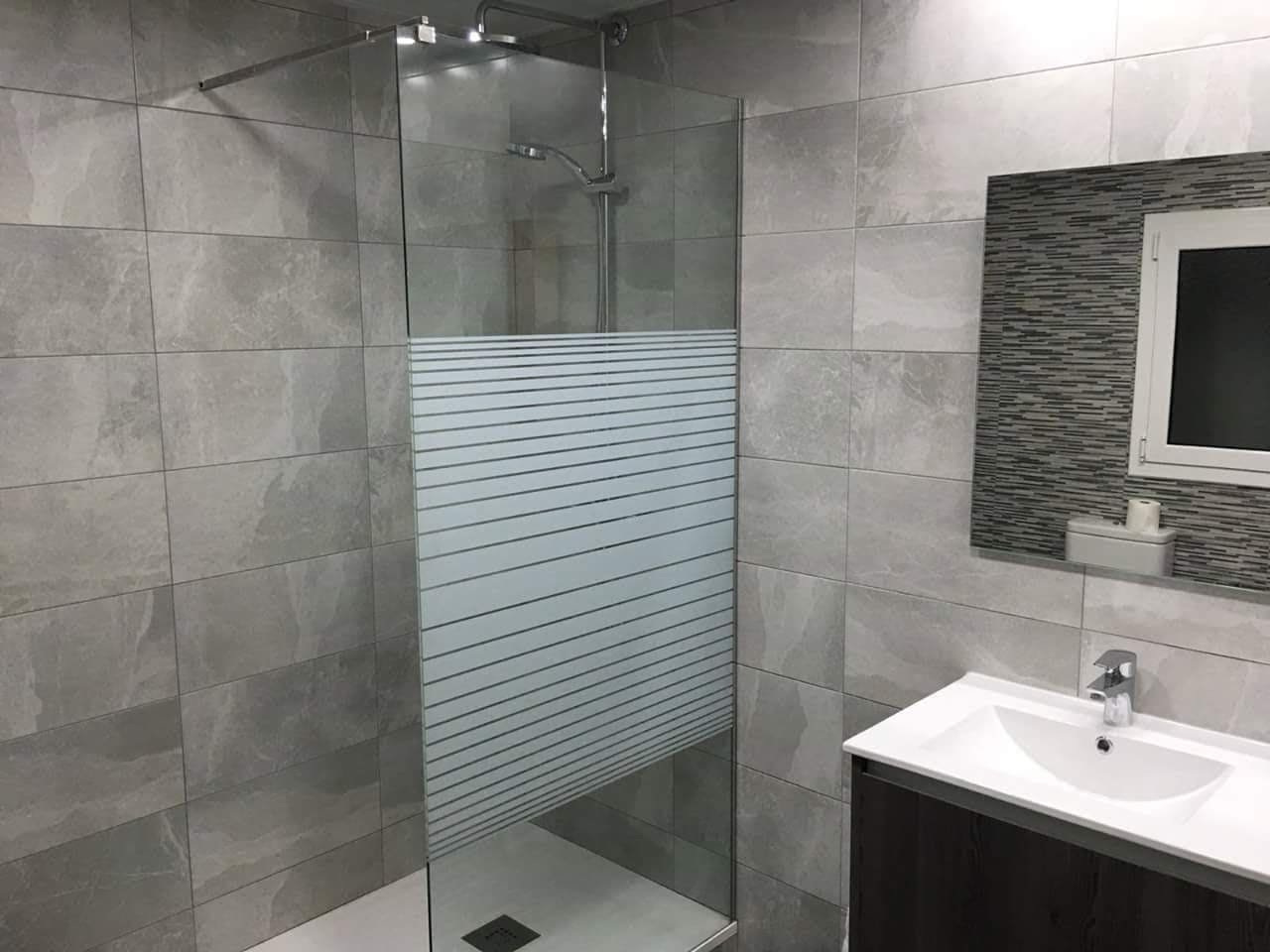 Reforma de baño con ducha amplia, mampara de vidrio y revestimiento gris