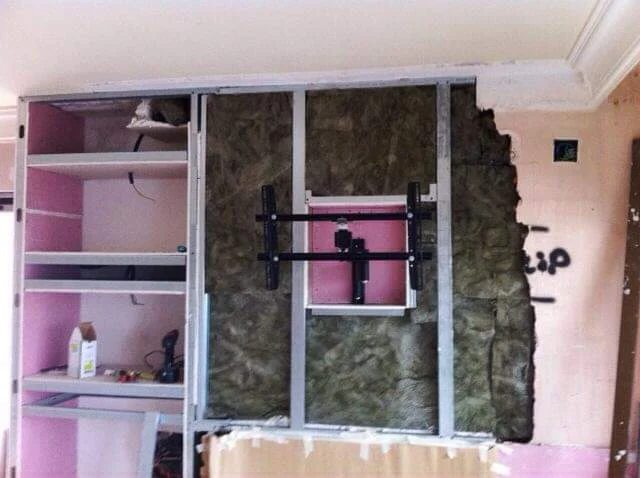 Proceso de construcción de un mueble de pladur a medida con estructura metálica, aislamiento interior y espacios integrados para televisión, chimenea y estanterías.