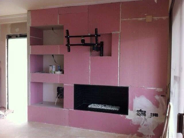 Fase de revestimiento del mueble a medida con placas de pladur, dejando preparados los huecos para la televisión, la chimenea decorativa y las estanterías laterales.