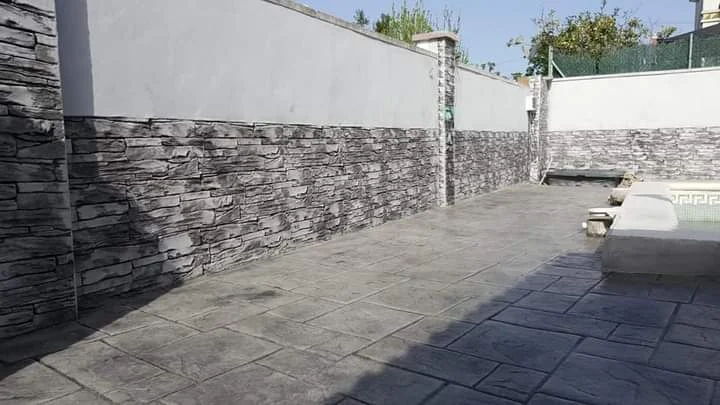 Acabado de pavimento exterior en hormigón impreso de color gris, combinado con revestimiento decorativo en los muros para crear un espacio uniforme, resistente y renovado.